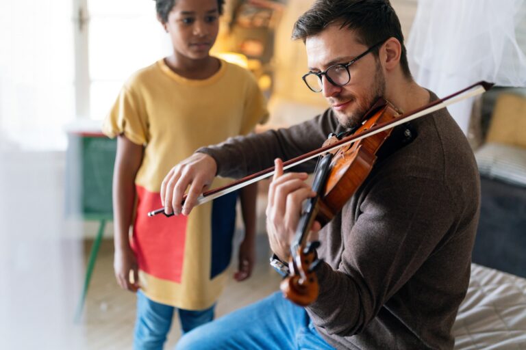Charming little girl learning to play the violin with an artistic music teacher.